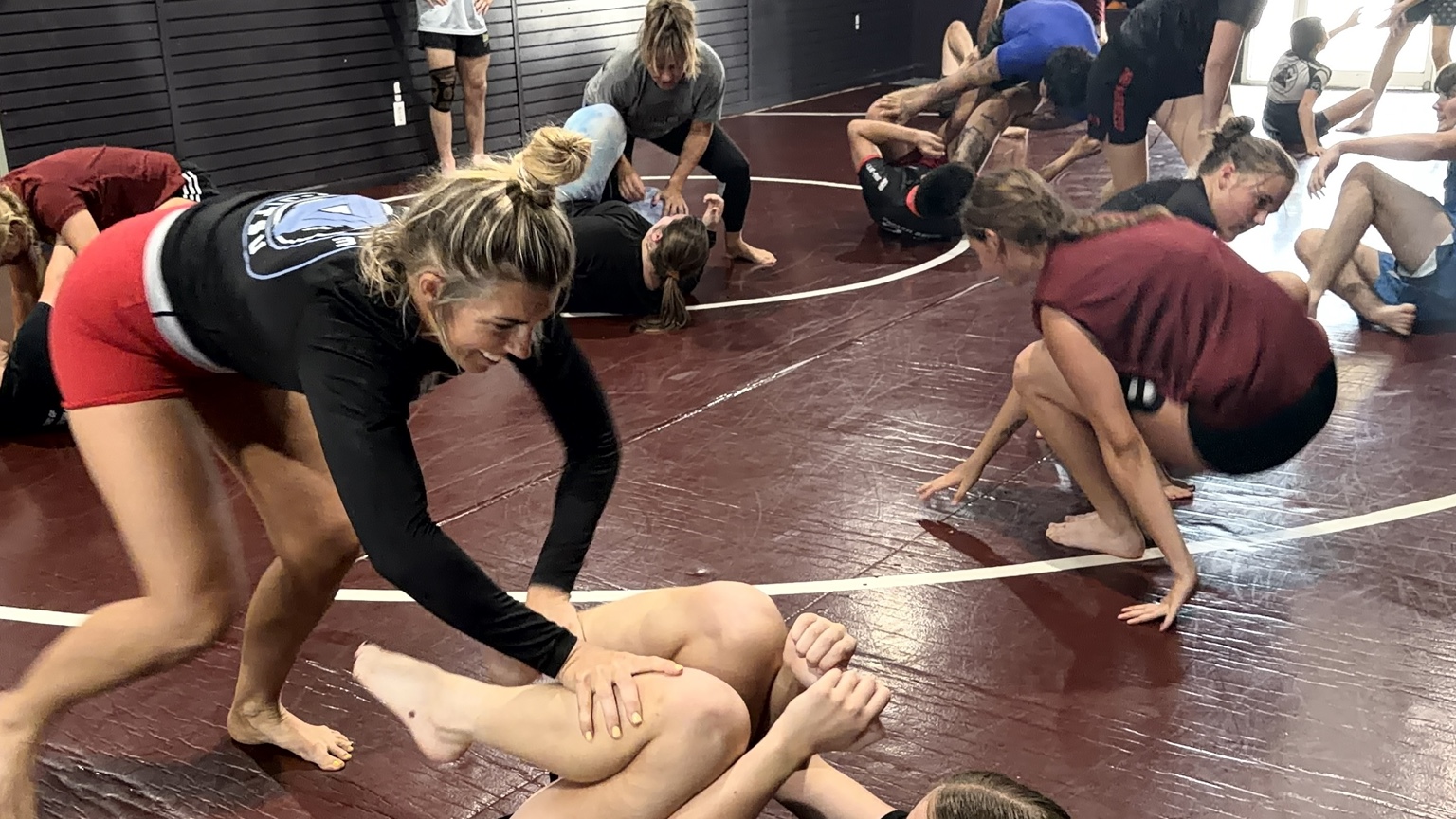 A smiling student in red shorts training during a live Force Jiu-Jitsu class