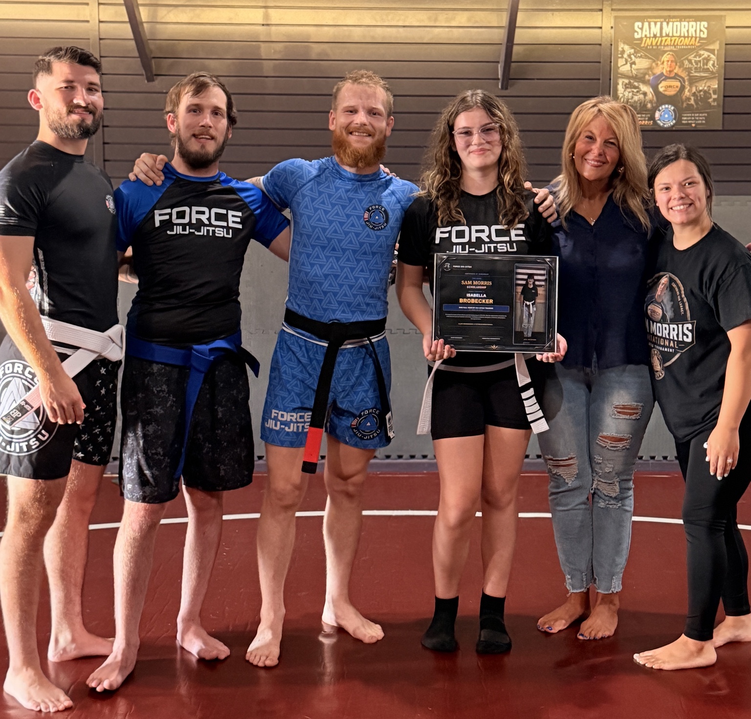 Isabella BroBecker holding her 2026 Sam Morris Scholarship certificate with the Force Jiu-Jitsu team and members of the Morris family